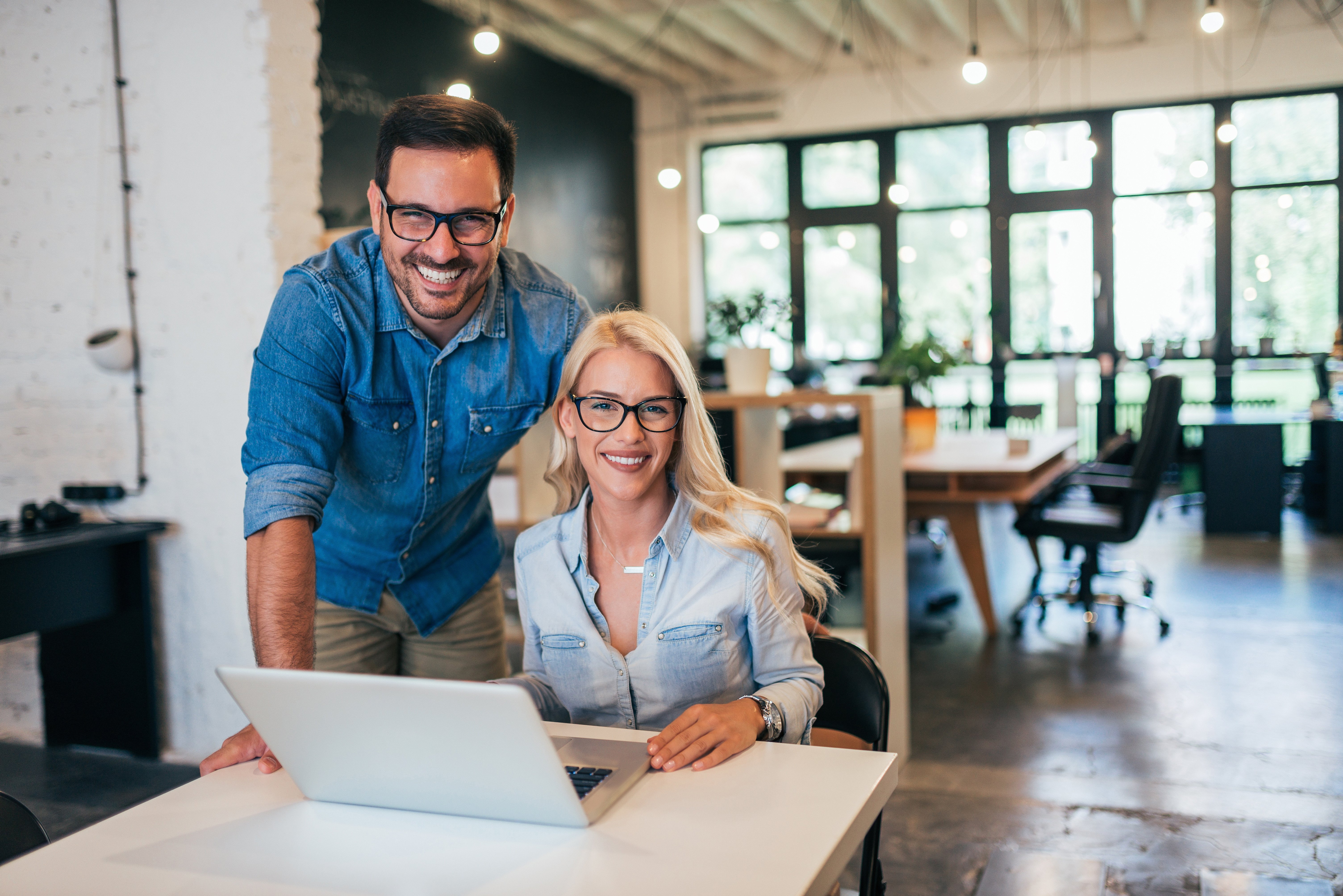 A man looking over his female business partner's shoulder, both smiling 