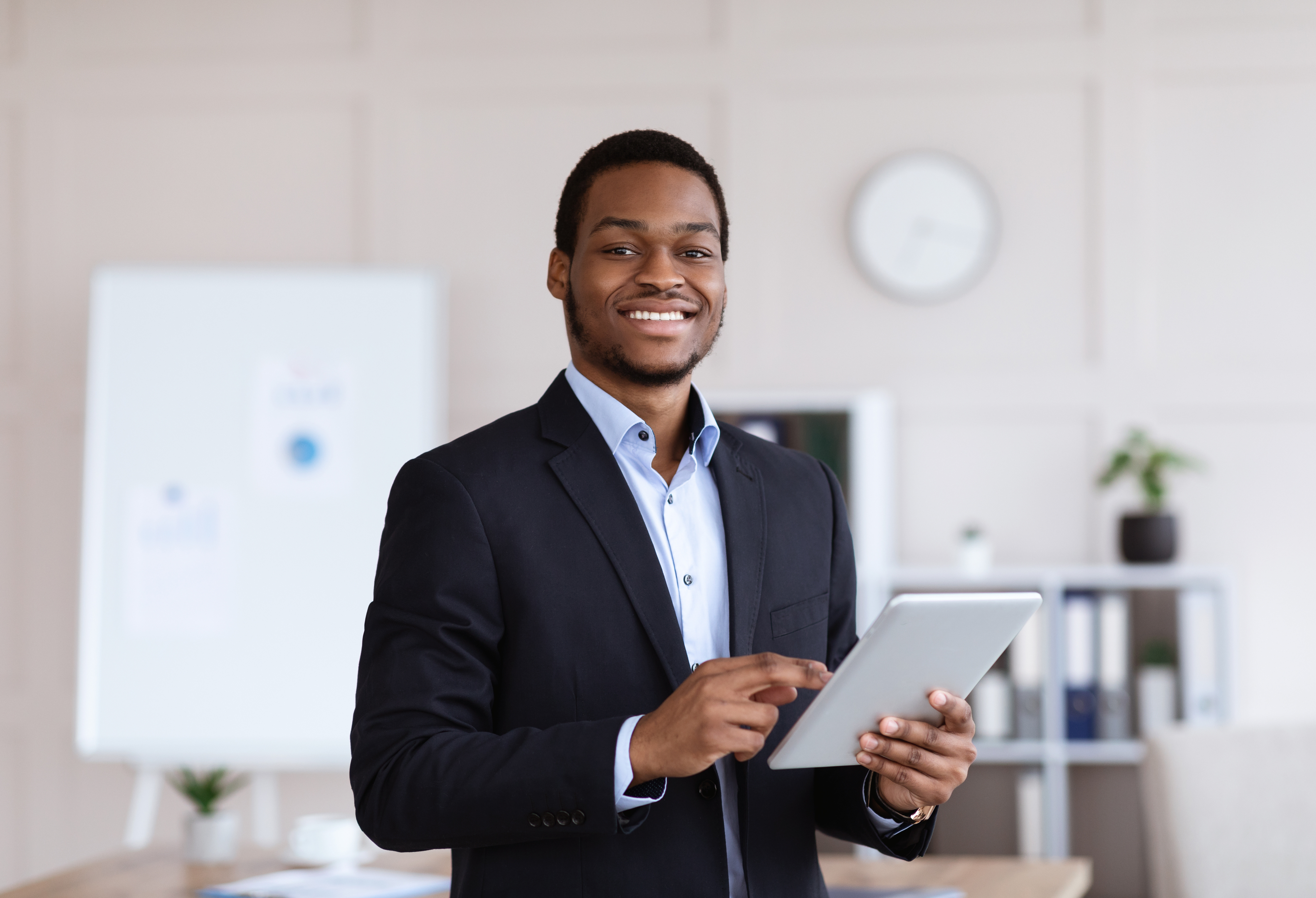 Man in suit, smiling, and holding tablet