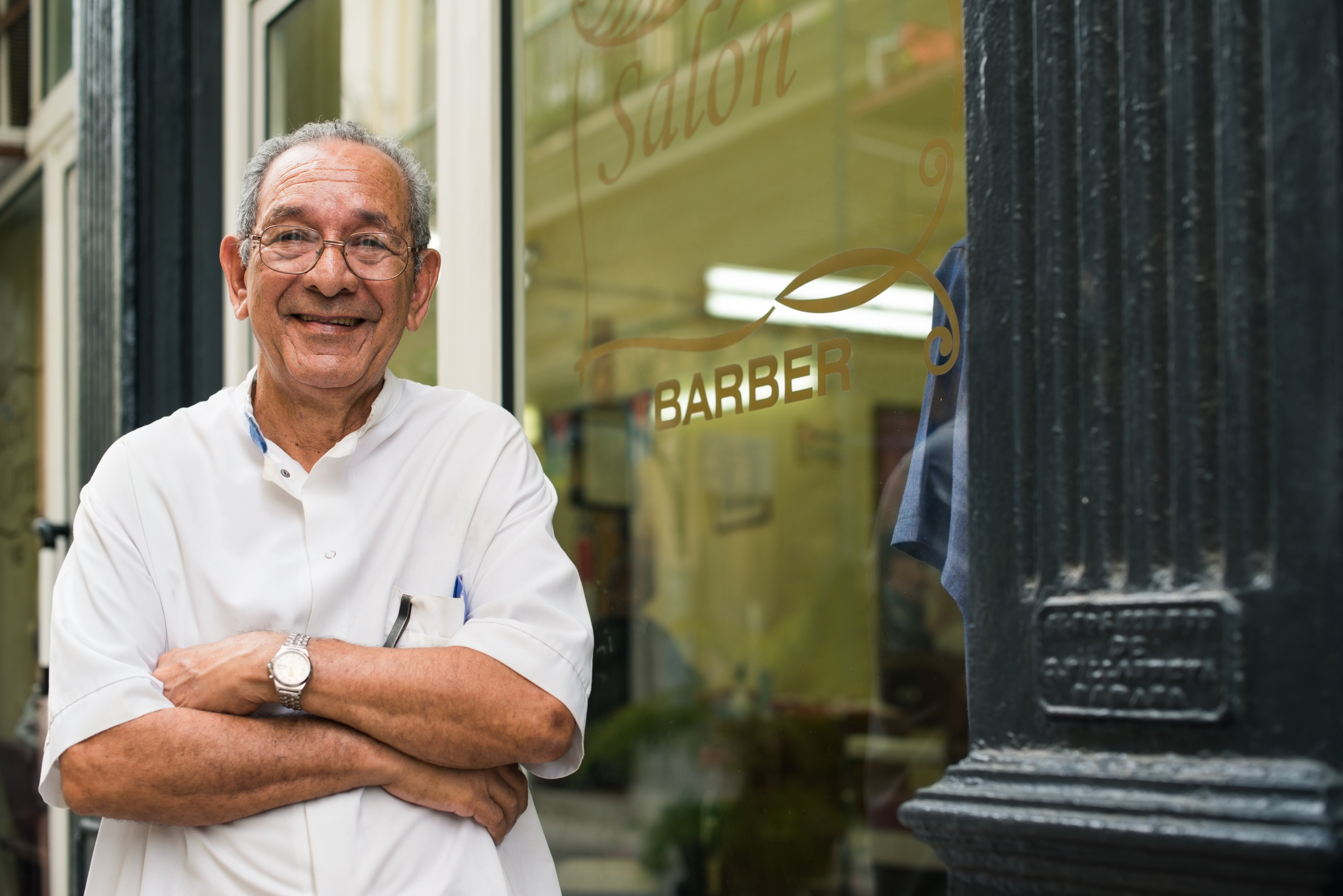 Elder man standing proudly outside his barber shop 