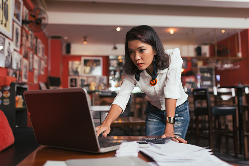 Woman business owner reviewing documents on laptop